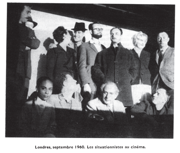 A black and white photo of Situationists sitting and standing in front of a cinema projection