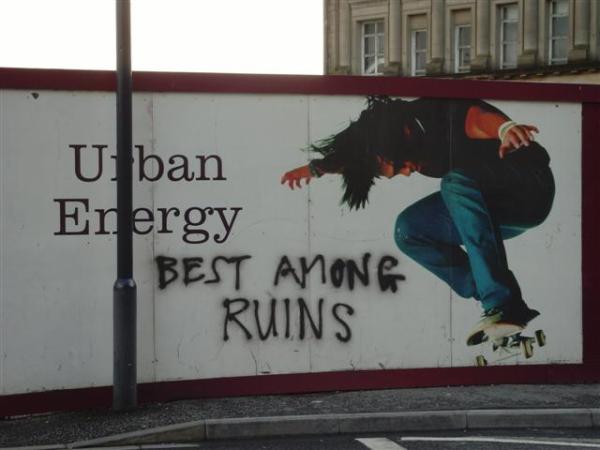 Billboard with the slogan "Urban Energy" and a skateboarder. Graffiti saying "Best Among Ruins" has been added