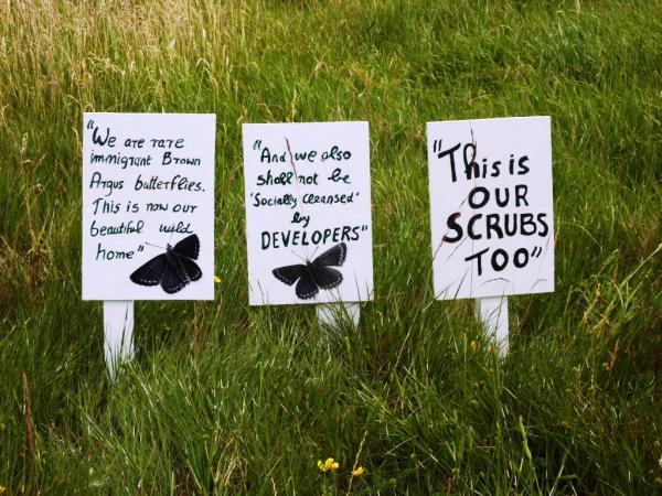 White placards with black text placed on Wormwood scrubs. Slogans include "this is our scrubs too!"