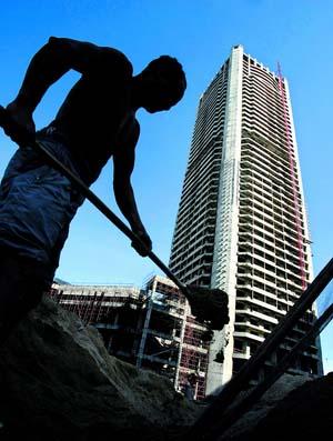 A chinese construction worker in the shadow of a high rise